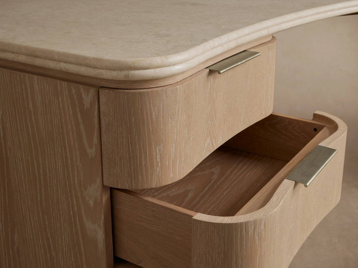 Caden Executive Desk with light oak veneer, a curved cream marble top, and 6 drawers with brushed nickel pulls.