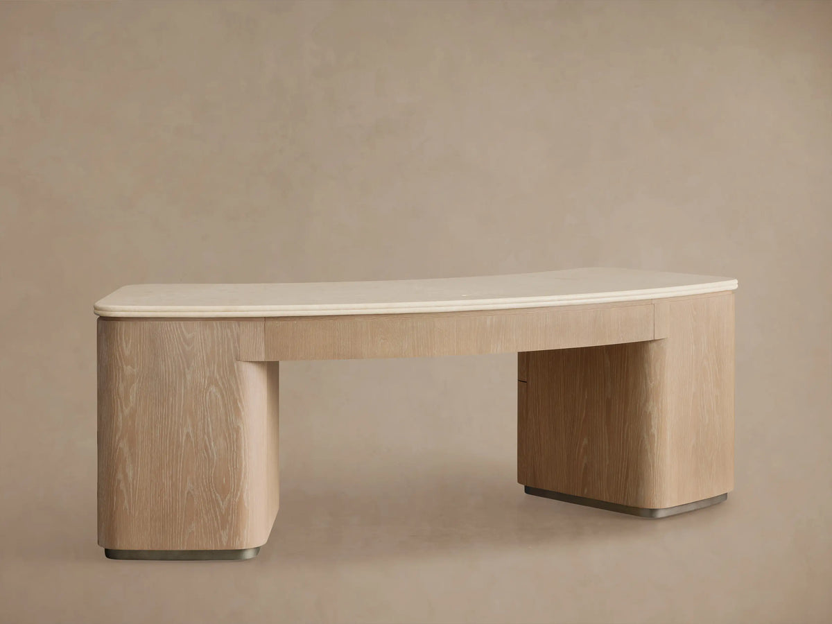 Close-up of Caden Executive Desk in Sand oak. Cream marble top with rounded edges. Bottom drawer partially open, brushed nickel pull.