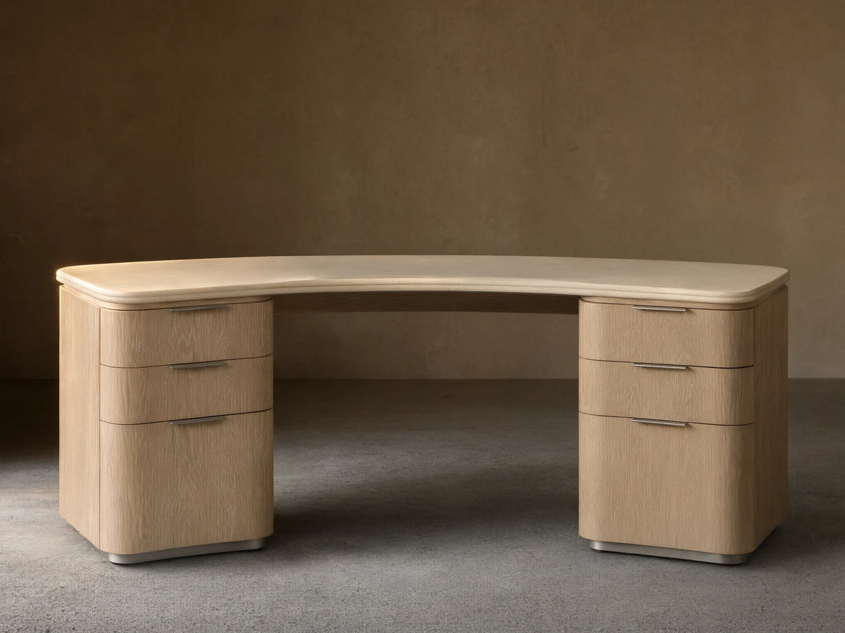 Caden Executive Desk. Light sand wood with rounded edges, cream marble top, and six drawers with brushed nickel hardware.