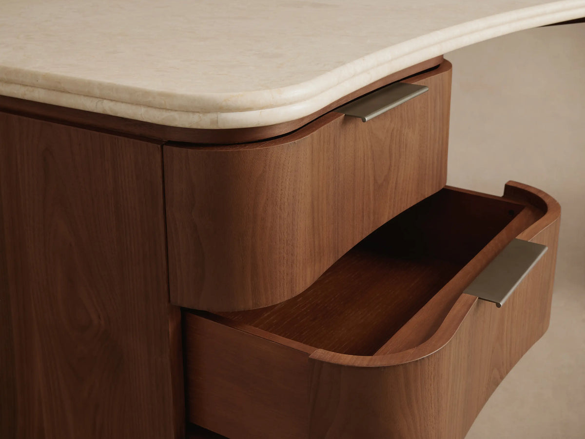 Caden Executive Desk: Walnut wood, curved cream stone top, rounded edges, 6 drawers with slim metallic pulls, plinth base.