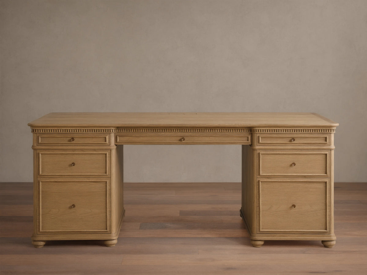 Full front view of a light Marcona-finished Carlisle Executive Desk. It features dentil molding, seven drawers with brass pulls, and bun feet.