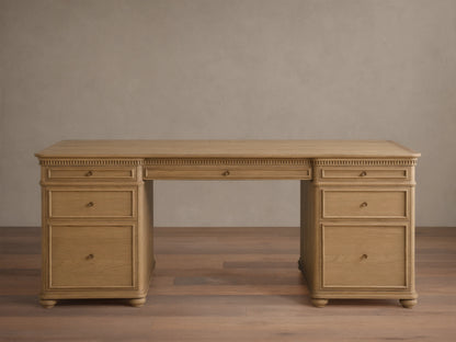Full front view of a light Marcona-finished Carlisle Executive Desk. It features dentil molding, seven drawers with brass pulls, and bun feet.