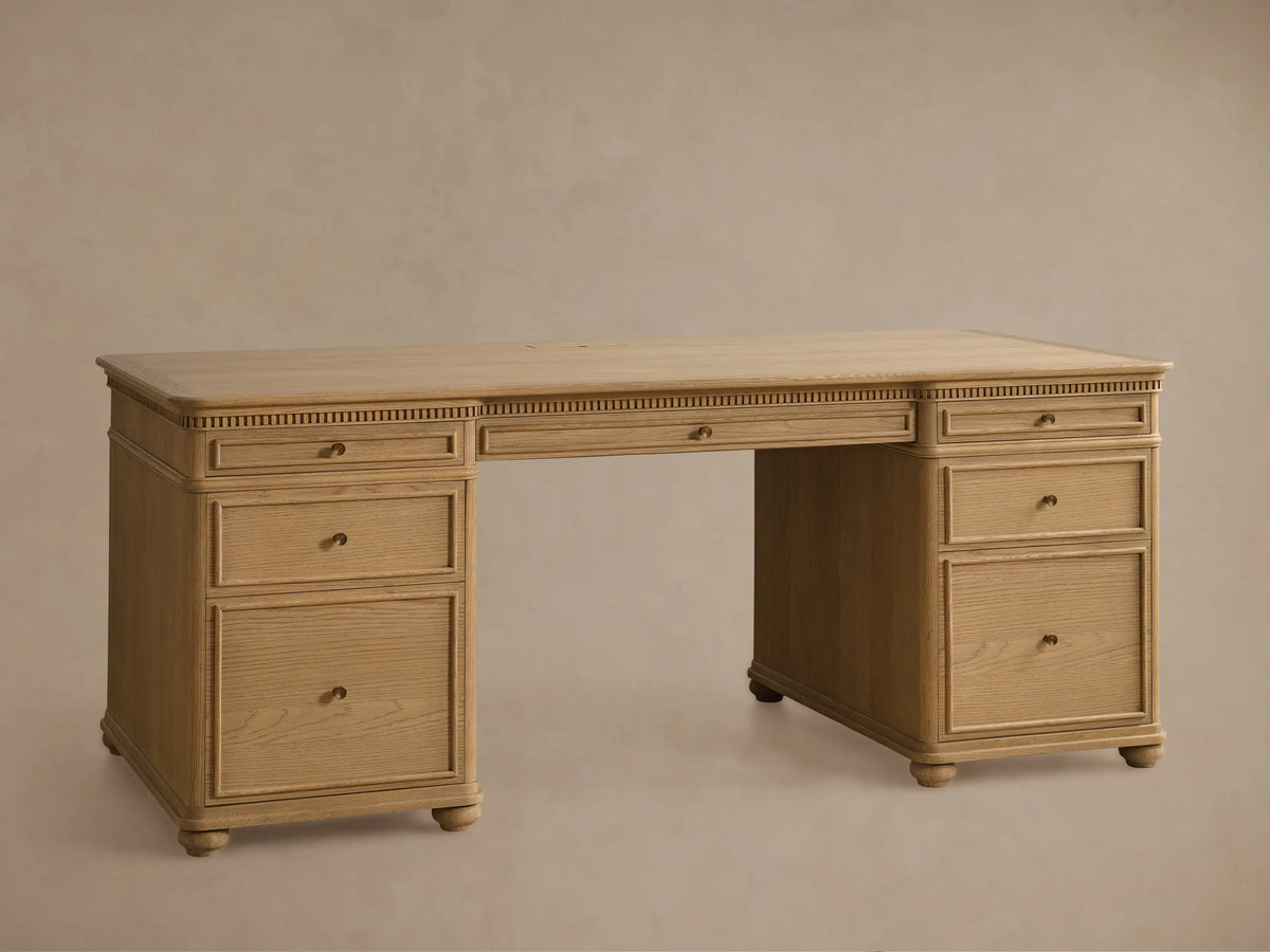 Full front view of a light Marcona-finished Carlisle Executive Desk. It features dentil molding, seven drawers with brass pulls, and bun feet.
