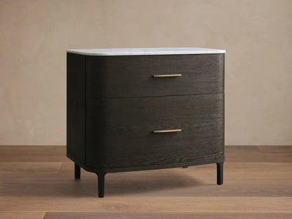 Front view of a dark brown wood two-drawer nightstand with curved sides, a white marble top, and brass pulls.