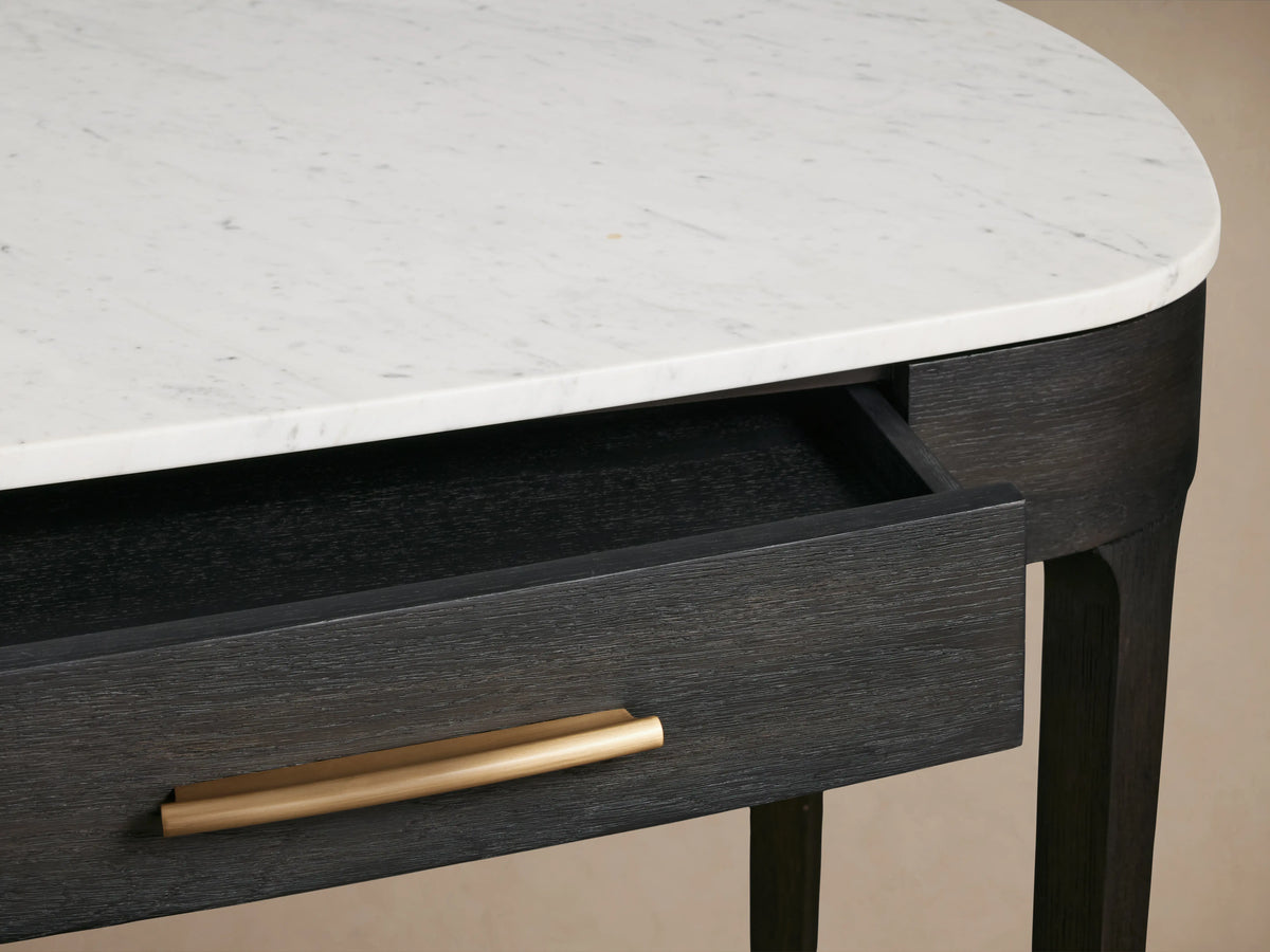 Close-up of Danny Writing Desk, showing its rounded white Carrara marble top & open ebony drawer with brass handle.