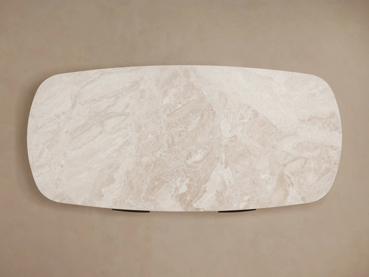 Top view of Danny Writing Desk. Rounded light beige marble top with natural veining and subtle texture on a warm, plain background.