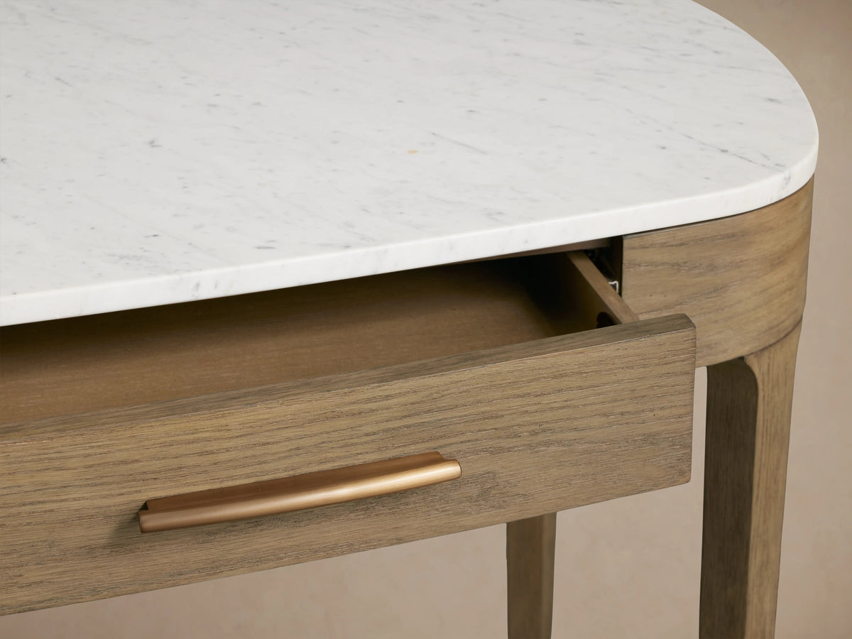 Angled close-up of Danny Writing Desk with white marble top, fawn wood frame. One drawer slightly open, showing ash interior & brass handle.