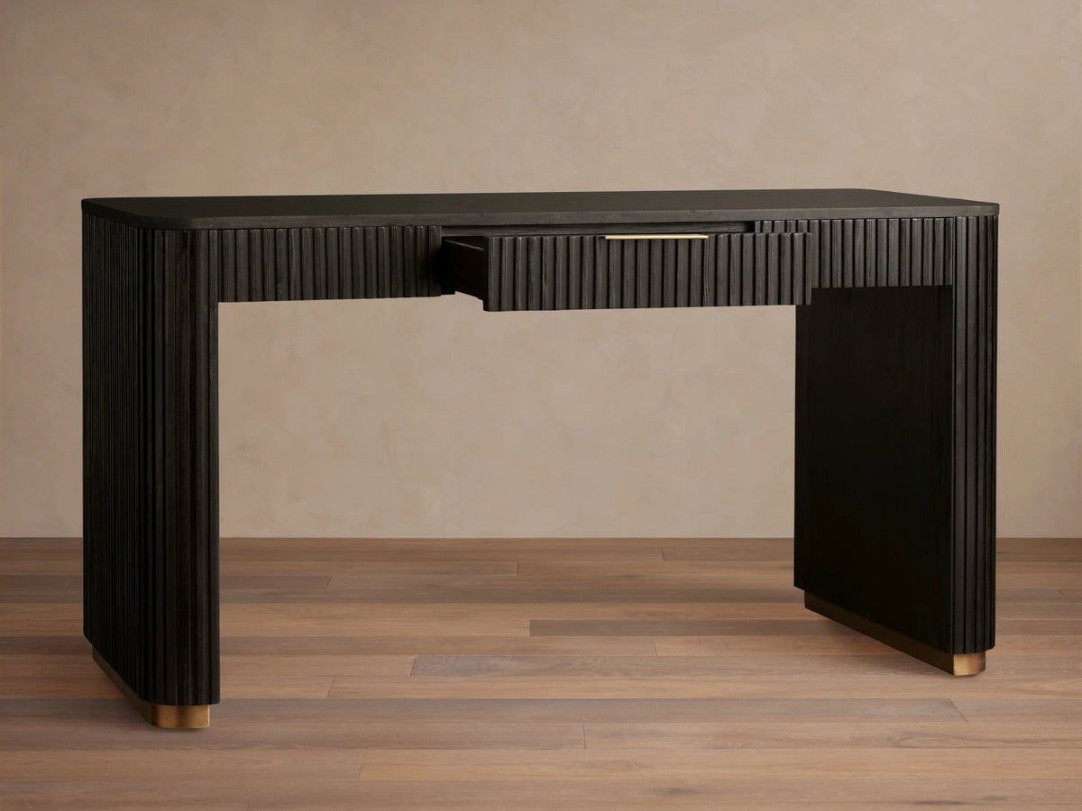 Finnley Writing Desk in dark wood finish, featuring reeded texture, light brass drawer pull, and gold-accented feet on a wooden floor.