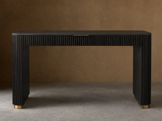 Finnley Writing Desk in dark wood finish, featuring reeded texture, light brass drawer pull, and gold-accented feet on a wooden floor.