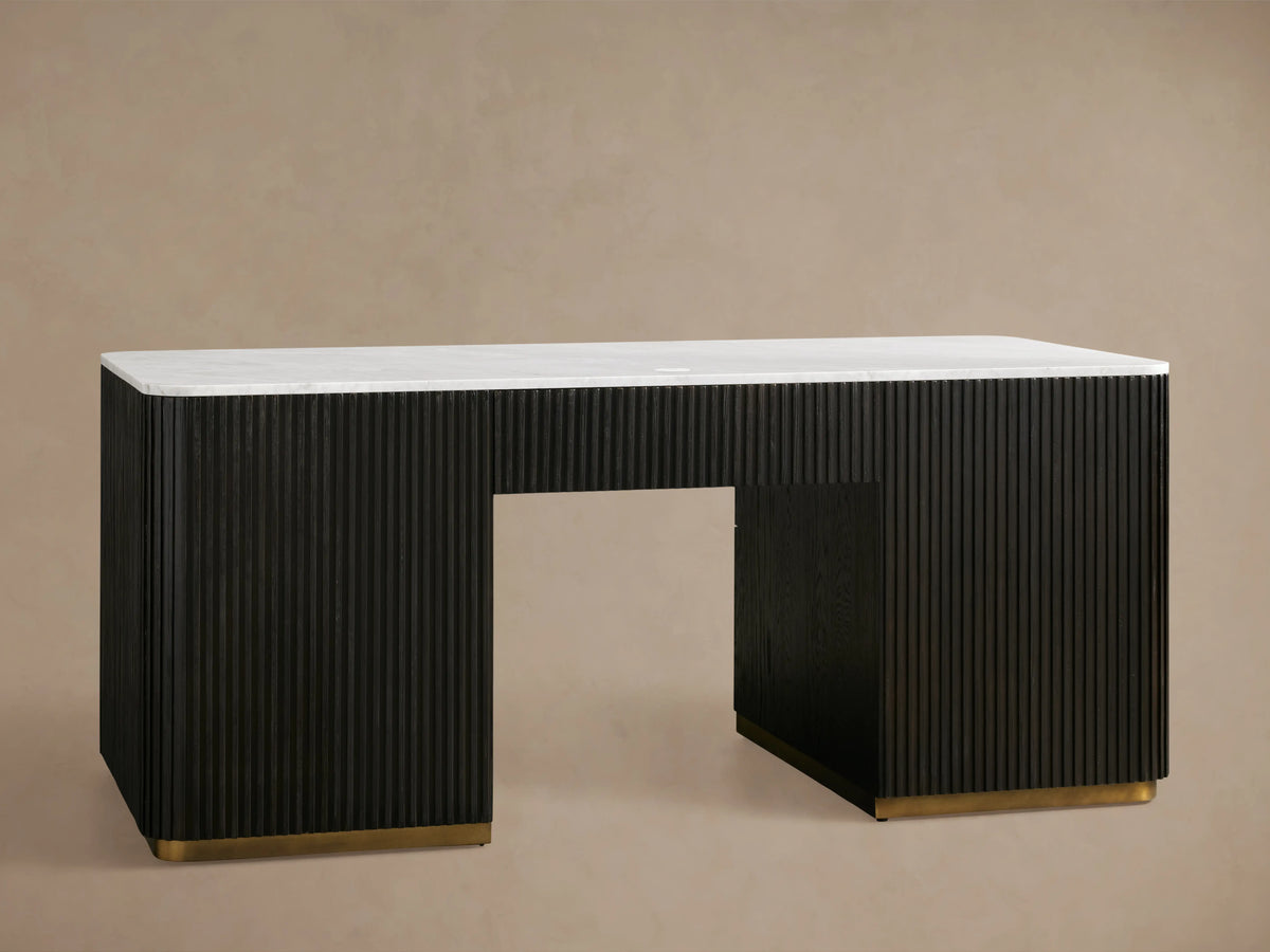 The Finnley Executive Desk features a reeded black wood base with three open drawers and brass handles, topped with a white surface.