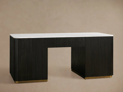 The Finnley Executive Desk features a reeded black wood base with three open drawers and brass handles, topped with a white surface.