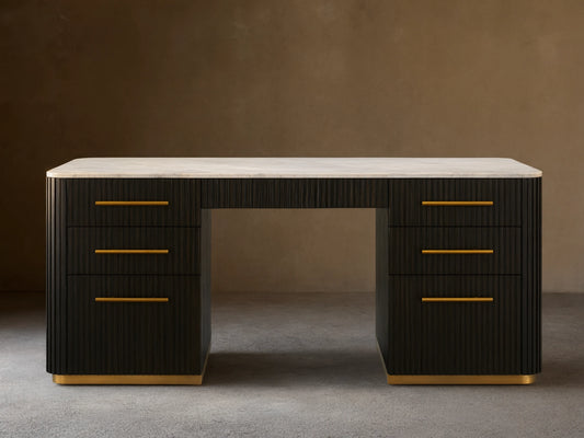 Finnley Executive Desk with dark wood finish, brass handles, six drawers, and a white surface, set on wood floor.