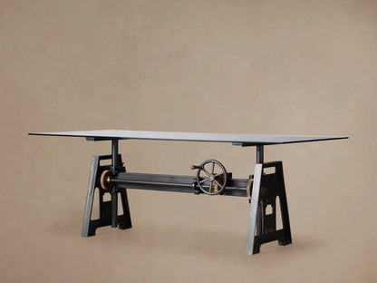 Industrial Crank Desk featuring a glass top on black rubbed copper base, with visible crank mechanism on wooden floor.