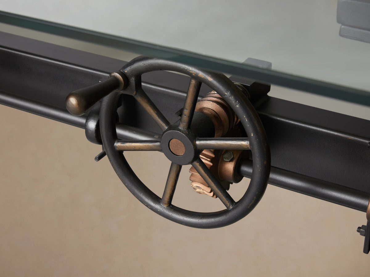 Industrial Crank Desk with glass top, side view showing black rubbed copper base, visible crank handle on left.