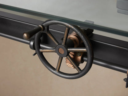Industrial Crank Desk with glass top, side view showing black rubbed copper base, visible crank handle on left.