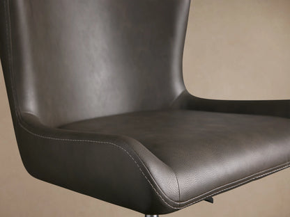 Kirsten Faux Leather Desk Chair with dark upholstery, curved backrest, and visible stitching on seat. Brown background.