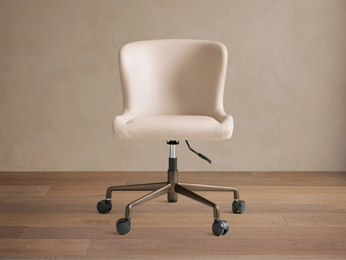 Kirsten Faux Leather Desk Chair, beige, angled slightly right on wood floor. Bronze powder-coated base with black casters.