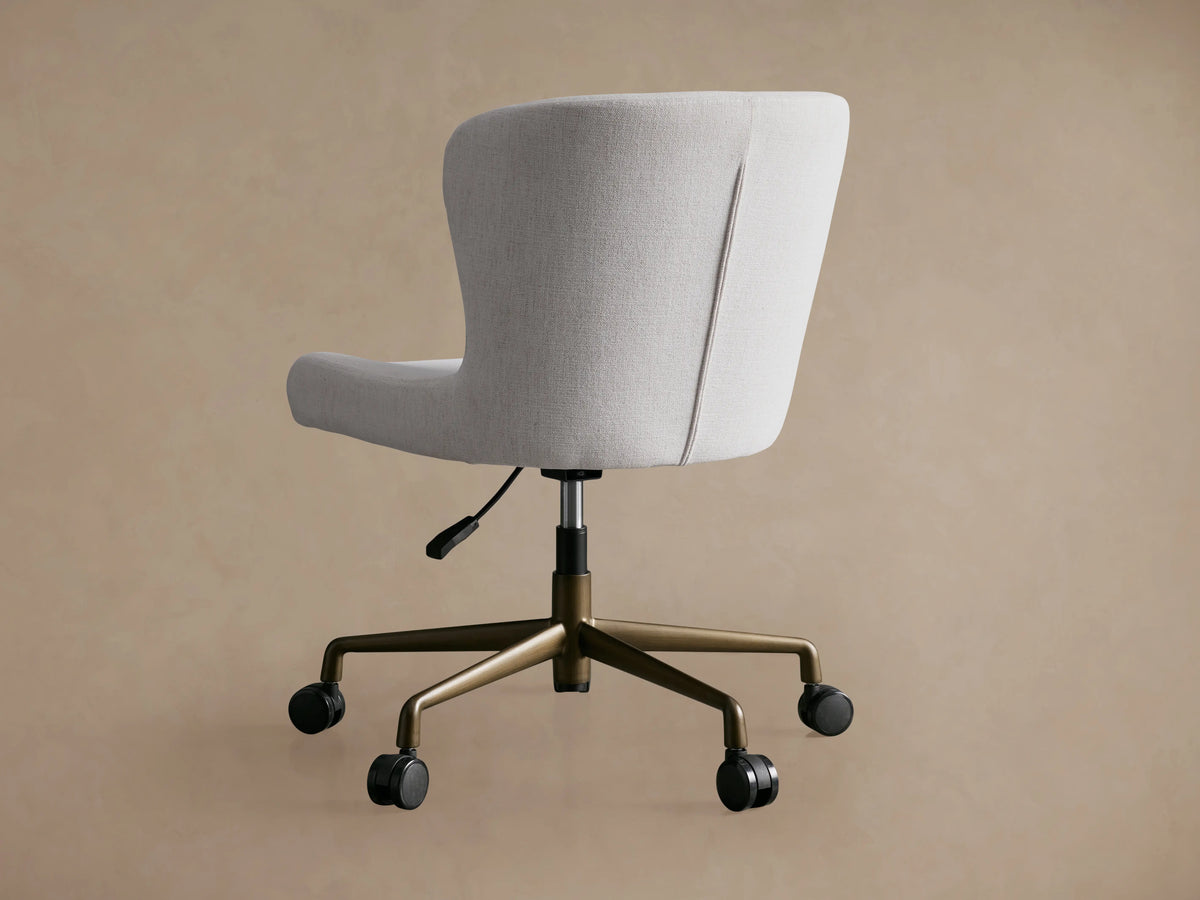 Kirsten Desk Chair with a white cushioned seat and backrest, gold powder-coated aluminum swivel base, and black casters on wood floor.