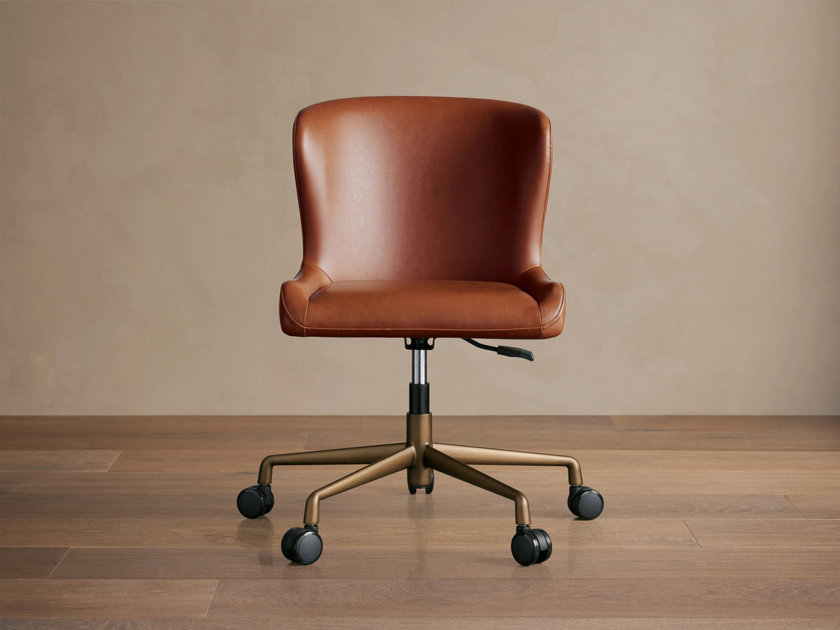 Kirsten Faux Leather Desk Chair in brown, featuring a curved backrest and seat. Swivel base on casters with bronze legs.