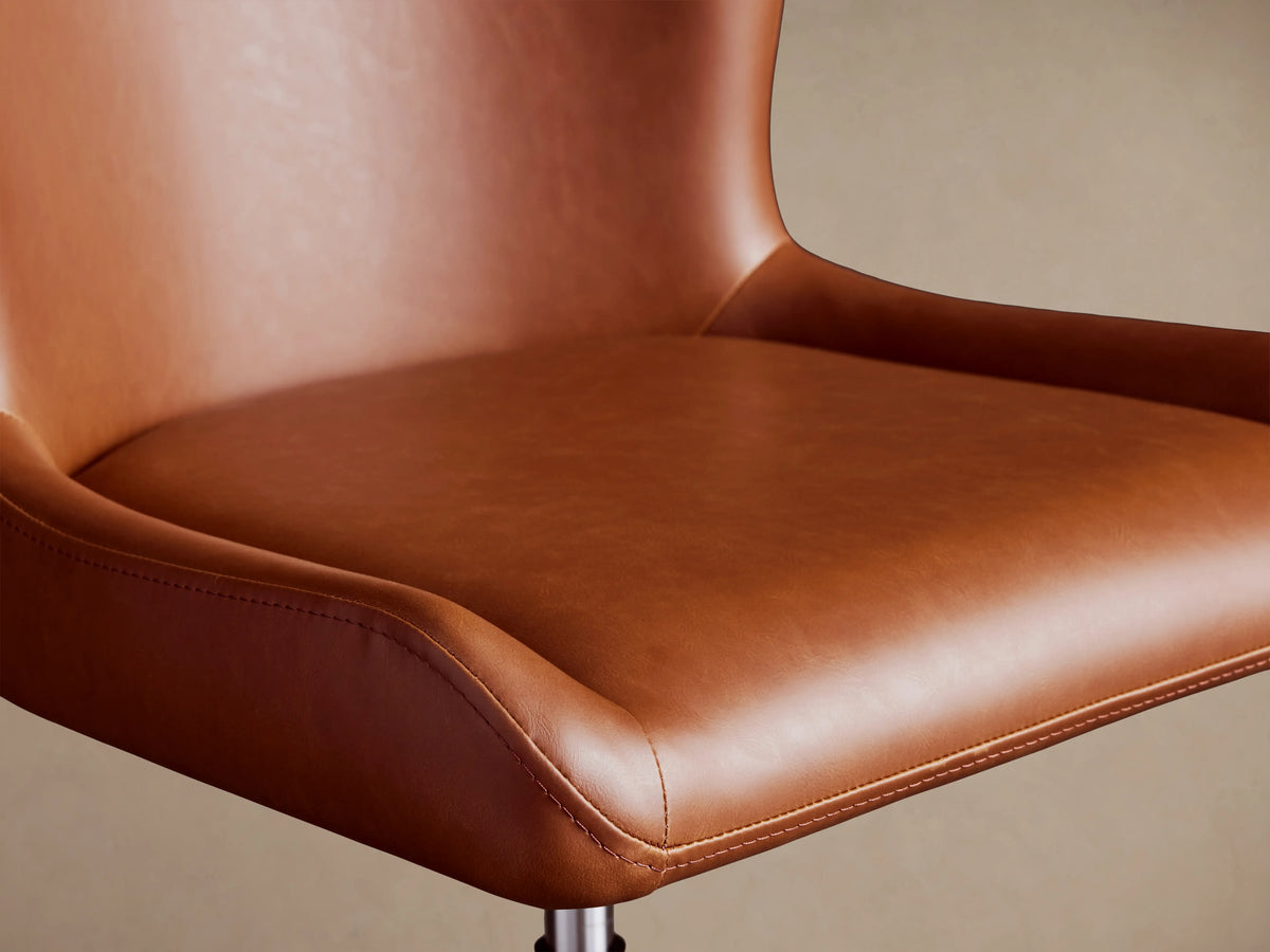 Kirsten Faux Leather Desk Chair in brown, close-up of seat and backrest. Smooth faux leather with gentle curves and visible stitching.