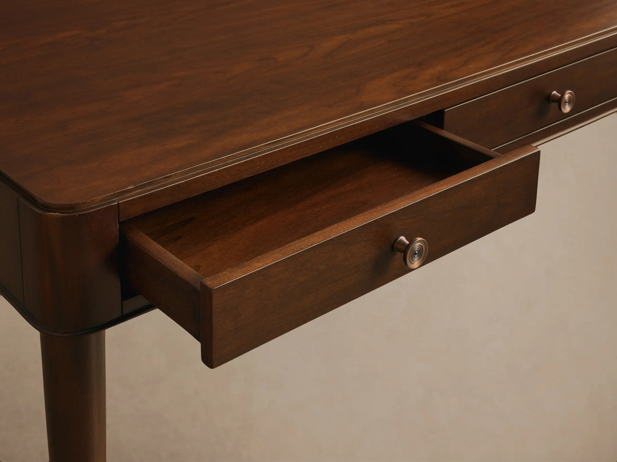 Close-up of a dark brown wooden desk with an open drawer, featuring a decorative brass-colored knob.