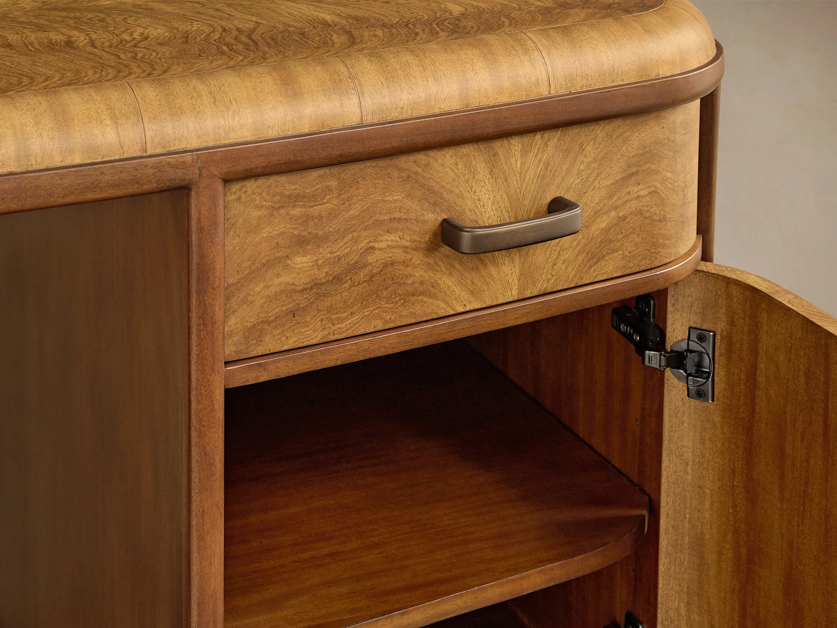Close-up of Palma Executive Desk. Warm cerajeira wood veneer desk with rounded top, open drawer, and bronze hardware.