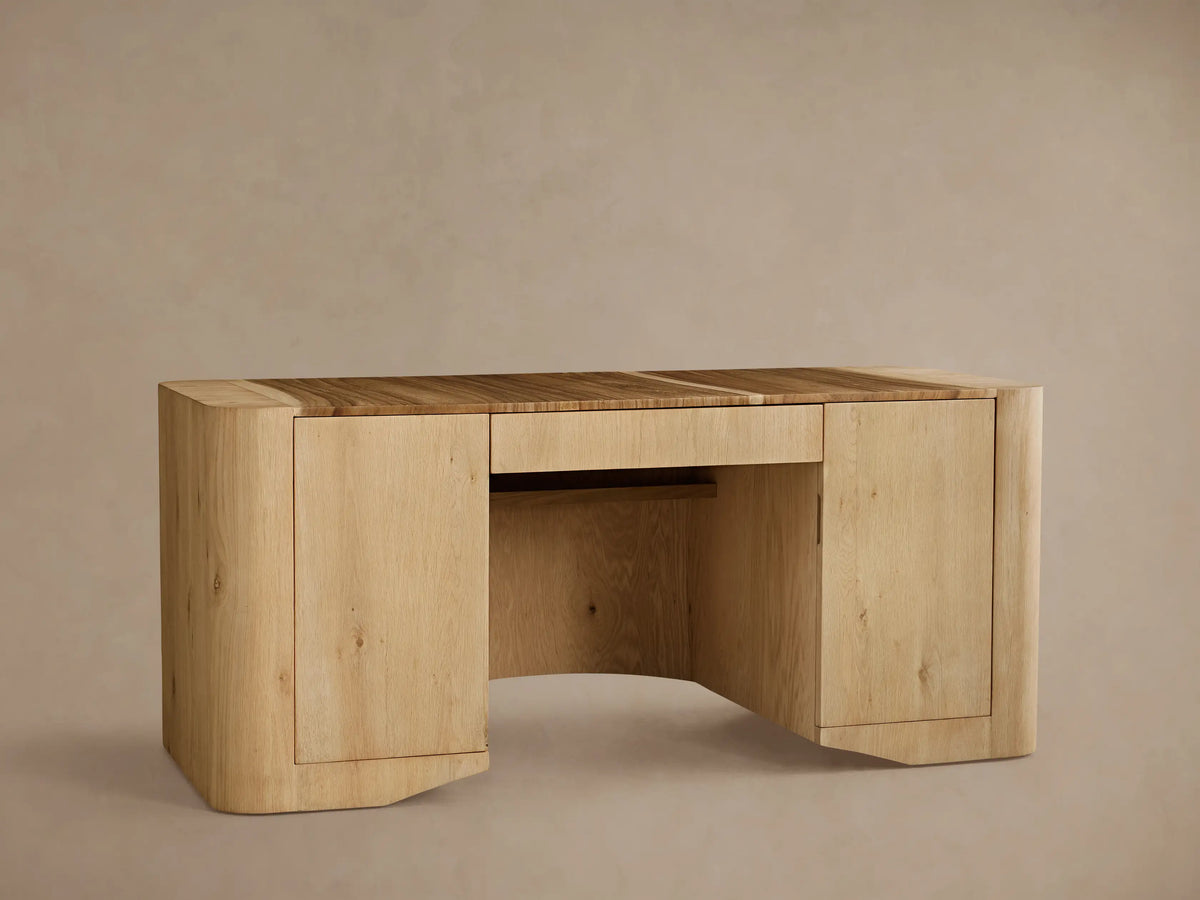 Front view of the Ramiro Executive Desk™ in light Guanacaste wood, featuring a curved front panel with prominent grain.