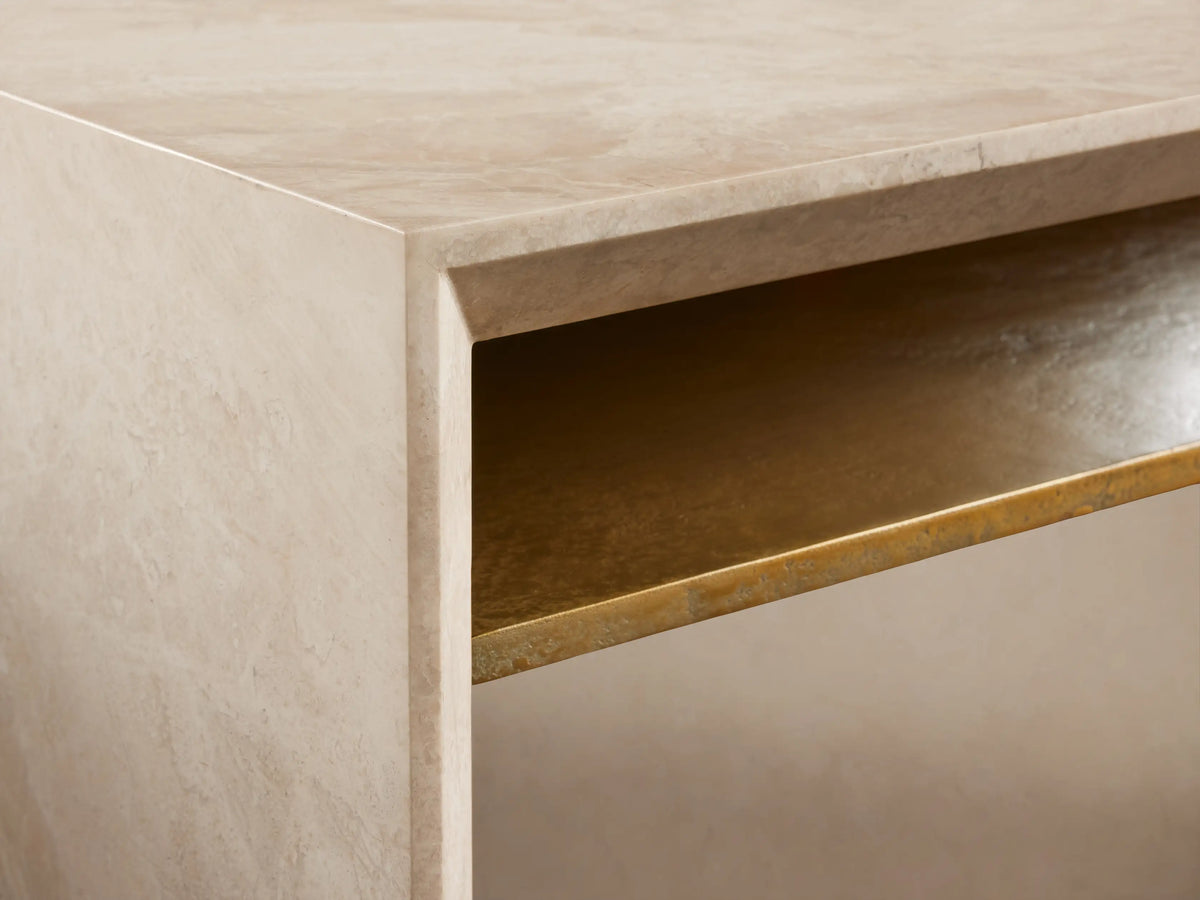 Sarsen Stone Desk with a smooth beige stone finish, rectangular top, and gold metal accent beneath. Set on a wooden floor.