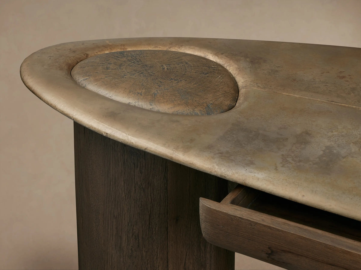 Sucurro Writing Desk: Dark spalted primavera wood legs hold an oxidized aluminum top with a brassy patina and central drawer.