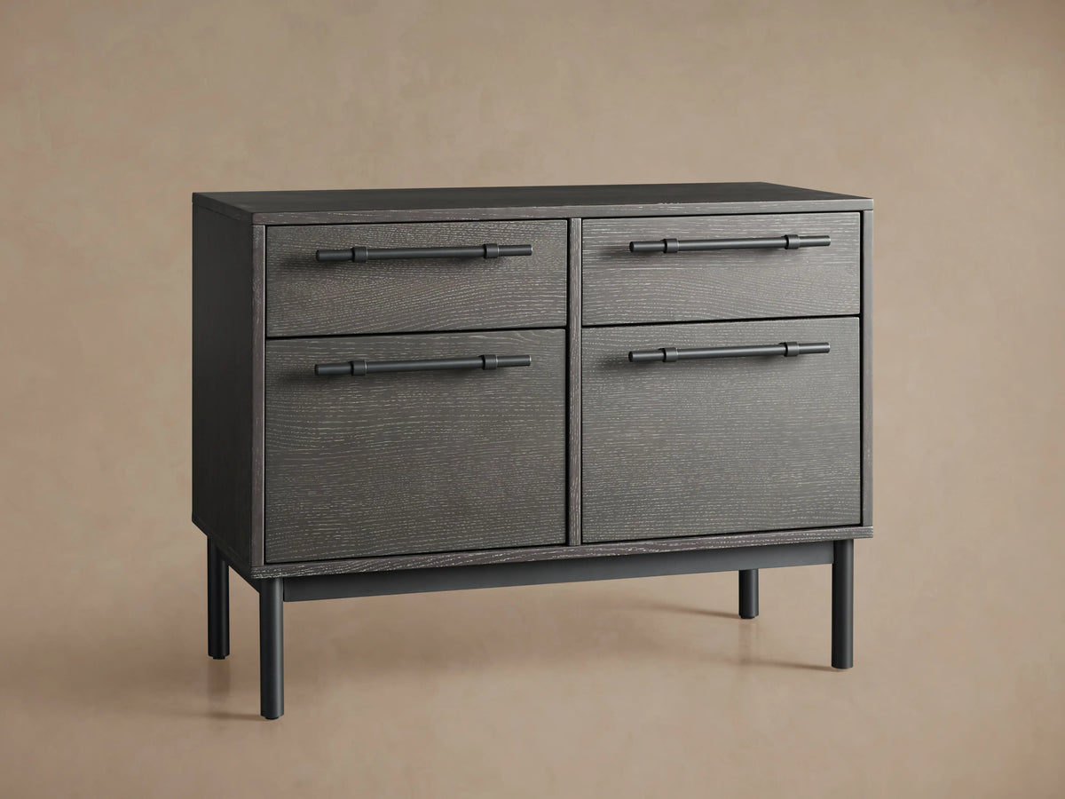 Sullivan File Cabinet in dark oak finish, featuring four drawers with black iron handles, set on slender black legs, displayed against a neutral wall.