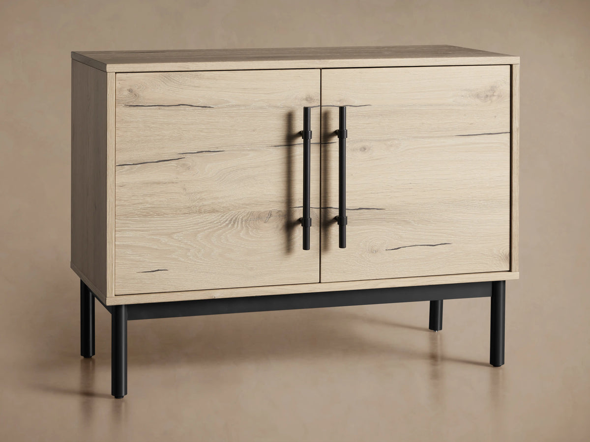 Sullivan Hall Chest in light oak with open and closed doors, black iron handles, and black metal legs on a beige background.