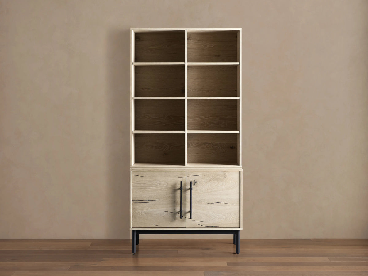 Sullivan Bookcase with Cabinet Base in light oak finish on hardwood floor, featuring upper shelves and lower cabinet with iron handles.