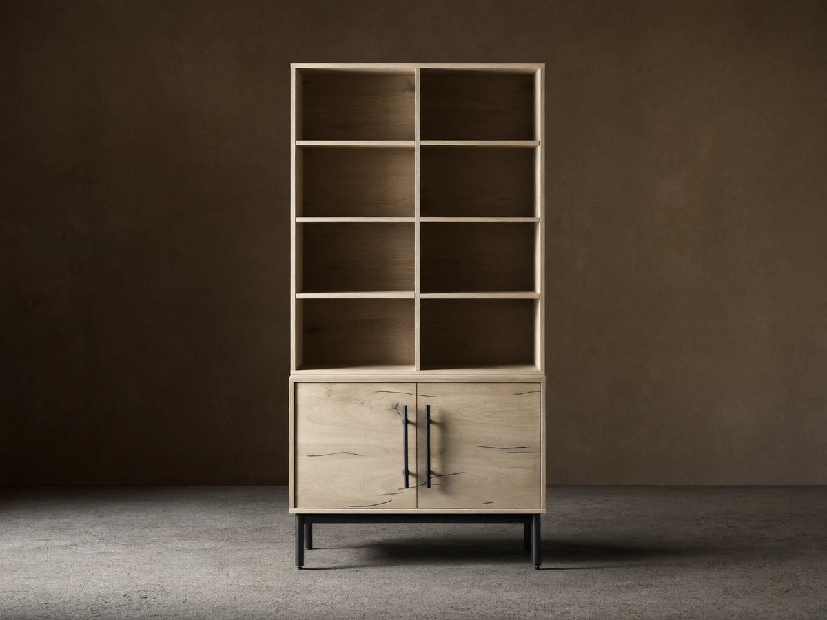 Sullivan Bookcase with Cabinet Base in light oak finish on hardwood floor, featuring upper shelves and lower cabinet with iron handles.
