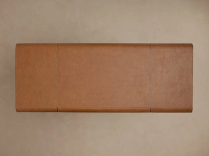 Brown leather corner of the Tullson Leather Desk with visible stitching, set on a brass base, against a beige background.