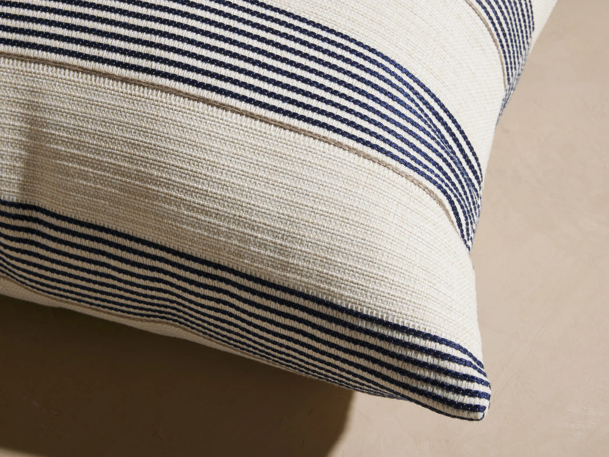 Dawson Outdoor Pillow, square, cream with woven horizontal navy and tan stripes, resting on a light outdoor sofa.