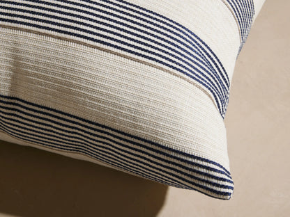 Dawson Outdoor Pillow, square, cream with woven horizontal navy and tan stripes, resting on a light outdoor sofa.