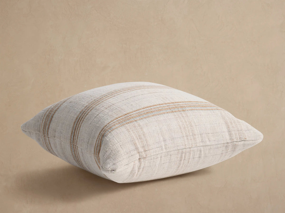 Brescia Outdoor Floor Pillow: Off-white woven pillow with thin tan horizontal stripes, shown angled on a light background.