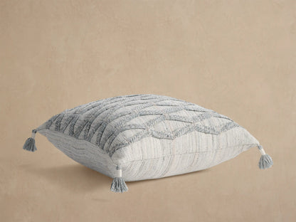 Mesa Outdoor Floor Pillow, light gray woven square with subtle vertical stripes & gray tassels on each corner, flat on tan.