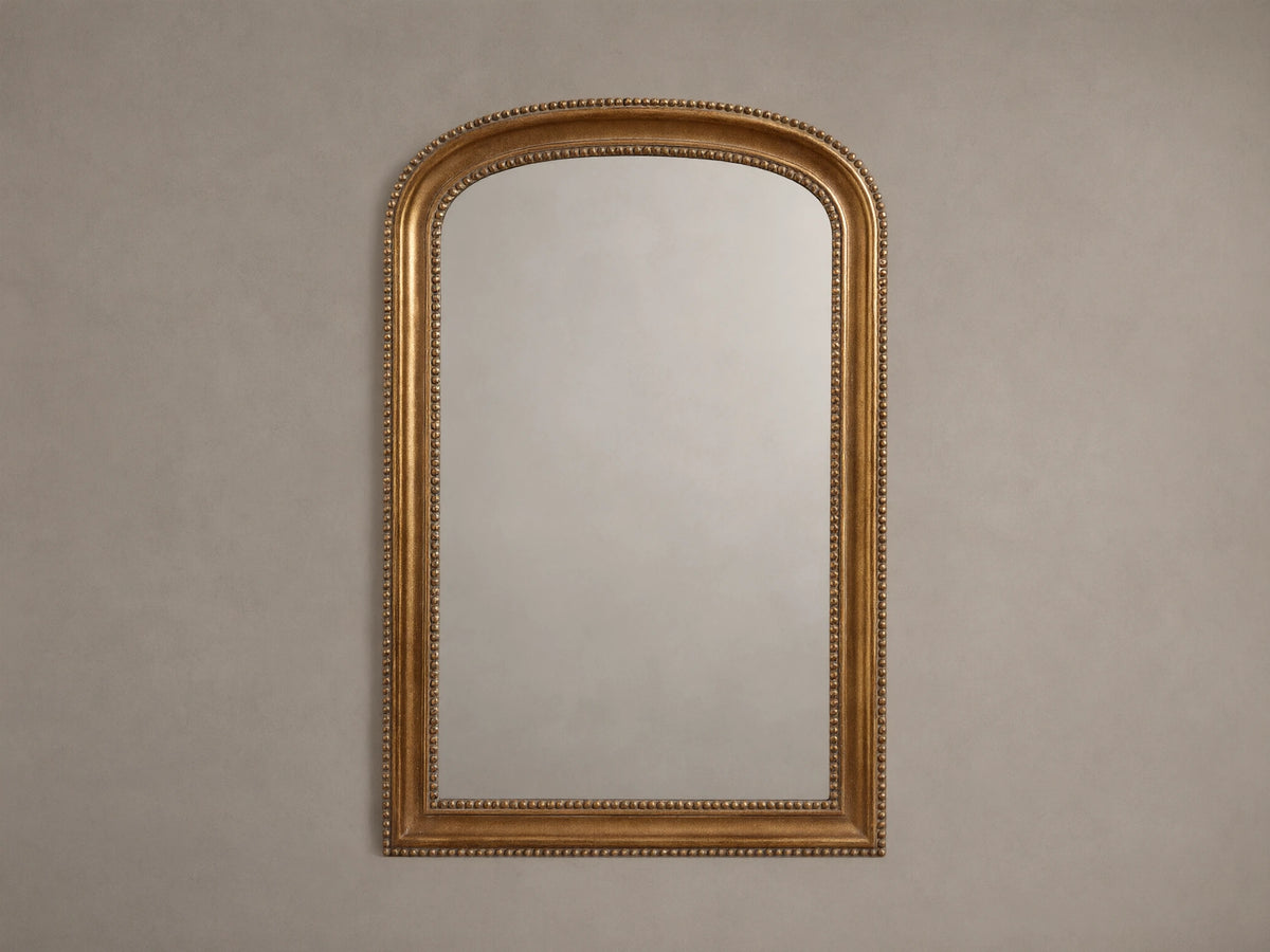 Pierre Bath Wall Mirror: arched-top, rectangular with a gold, beaded frame, hanging vertically on a neutral wall.