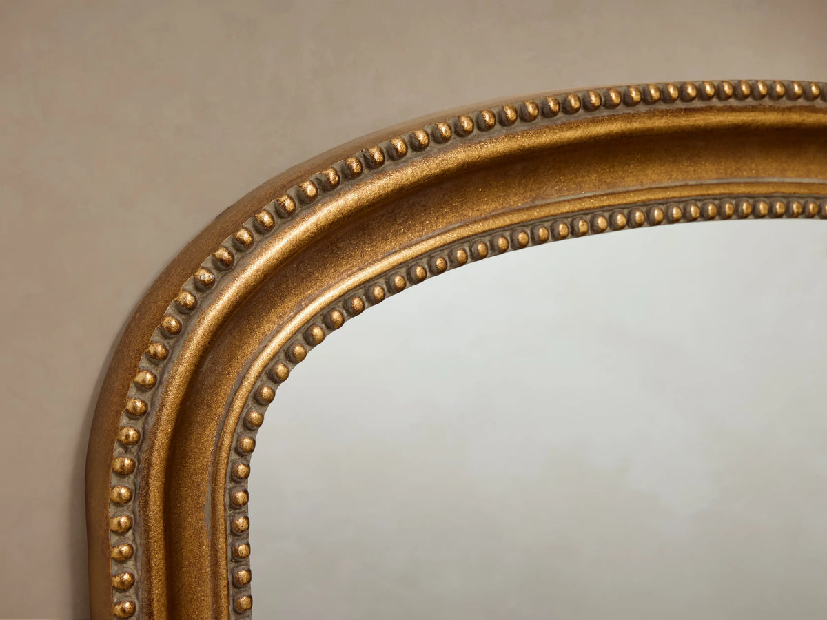 Pierre Bath Wall Mirror: arched-top, rectangular with a gold, beaded frame, hanging vertically on a neutral wall.