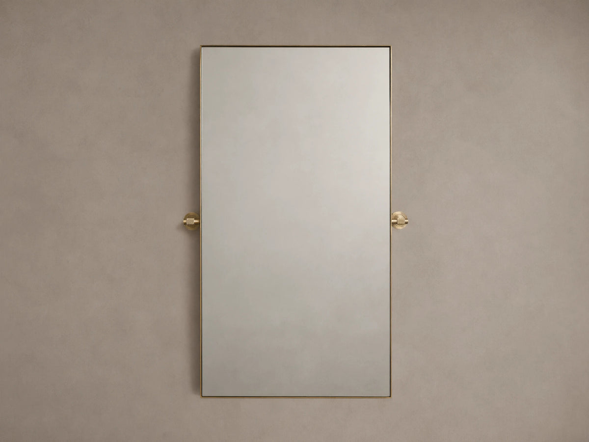 Monroe Bath Rectangular Wall Mirror in Brass with a slim brass frame, mounted against a beige wall with brass side accents.