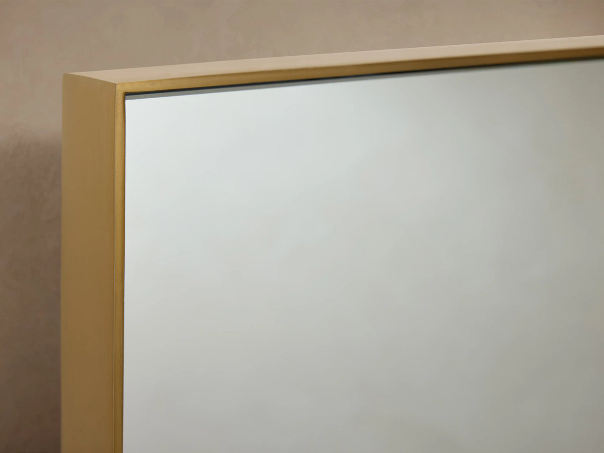 Monroe Bath Rectangular Wall Mirror in Brass with a slim brass frame, mounted against a beige wall with brass side accents.