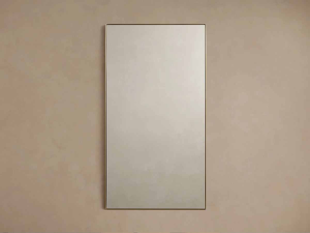 Lira Rectangular Bath Wall Mirror with a thin brass frame, hanging vertically against a neutral beige wall.