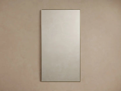 Lira Rectangular Bath Wall Mirror with a thin brass frame, hanging vertically against a neutral beige wall.