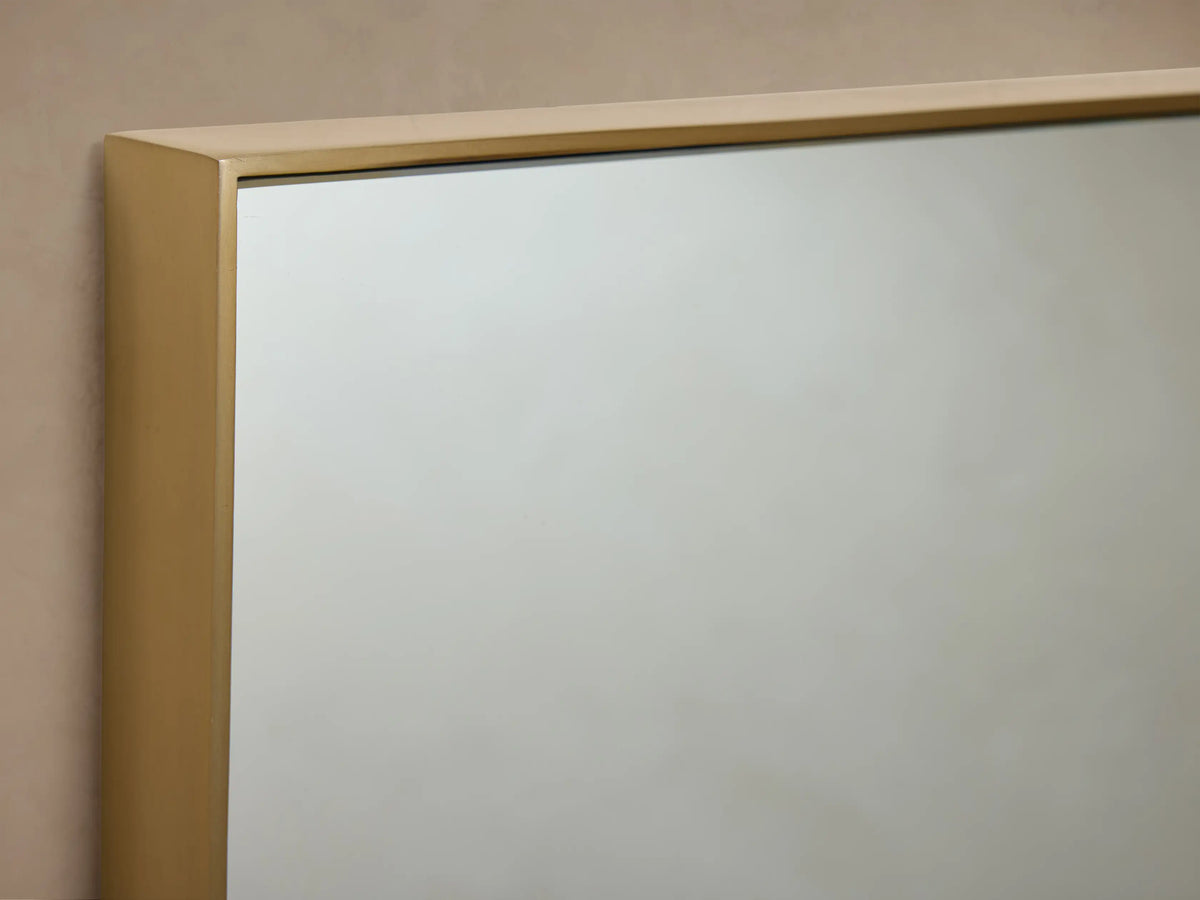 Lira Rectangular Bath Wall Mirror with a thin brass frame, hanging vertically against a neutral beige wall.