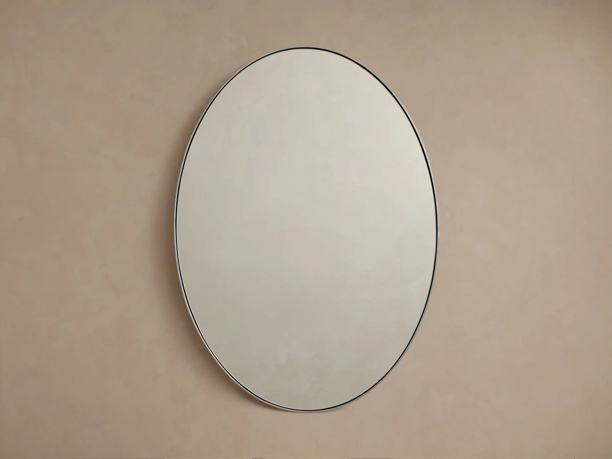 Oval wall mirror with a sleek nickel frame, reflecting a soft, neutral-colored wall backdrop.