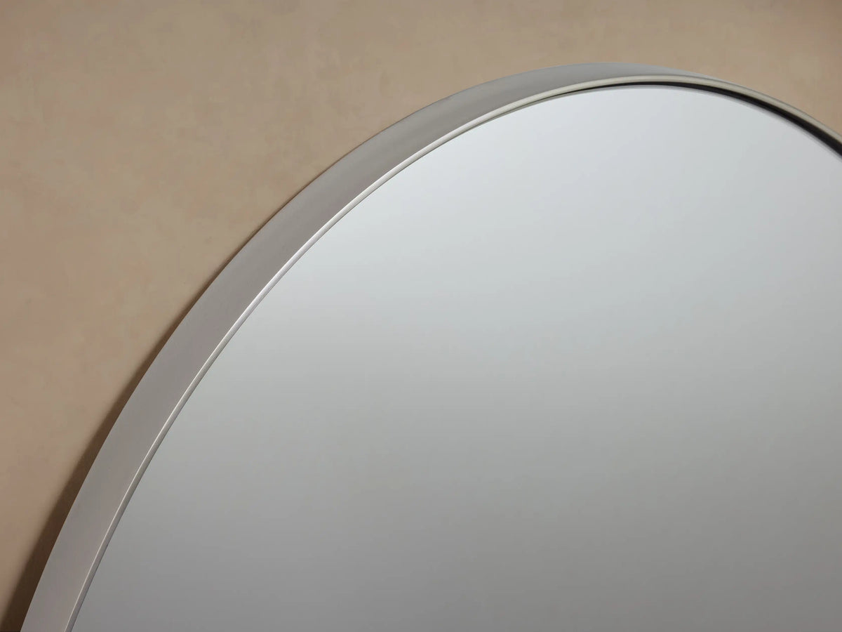 Oval wall mirror with a sleek nickel frame, reflecting a soft, neutral-colored wall backdrop.