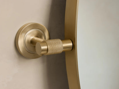 Round wall mirror with a slim brass frame. The reflective surface captures a subtle, blurred background.
