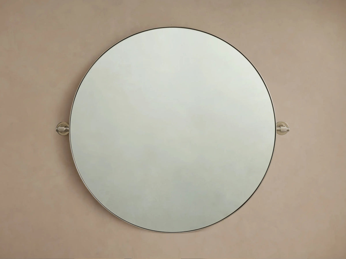 Round wall-mounted mirror with a thin metal frame, set against a beige background, featuring decorative knobs on each side.