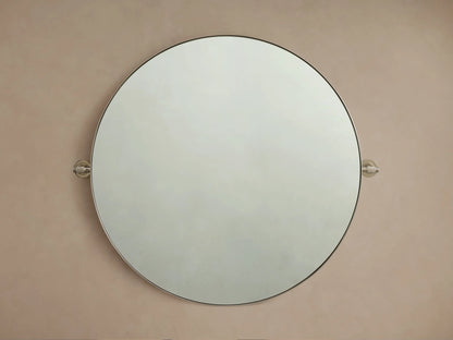 Round wall-mounted mirror with a thin metal frame, set against a beige background, featuring decorative knobs on each side.